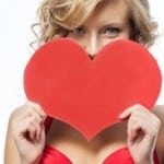 woman holds up red heart shape for Valentine's Day