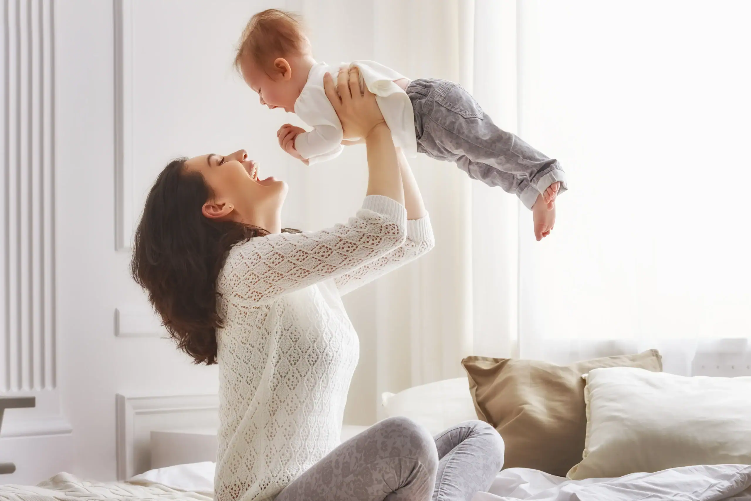 Happy woman holds her baby over her head., staring into his face.