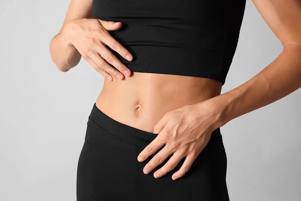 Close up of flat tummy and belly button on woman in black workout bra and tights.