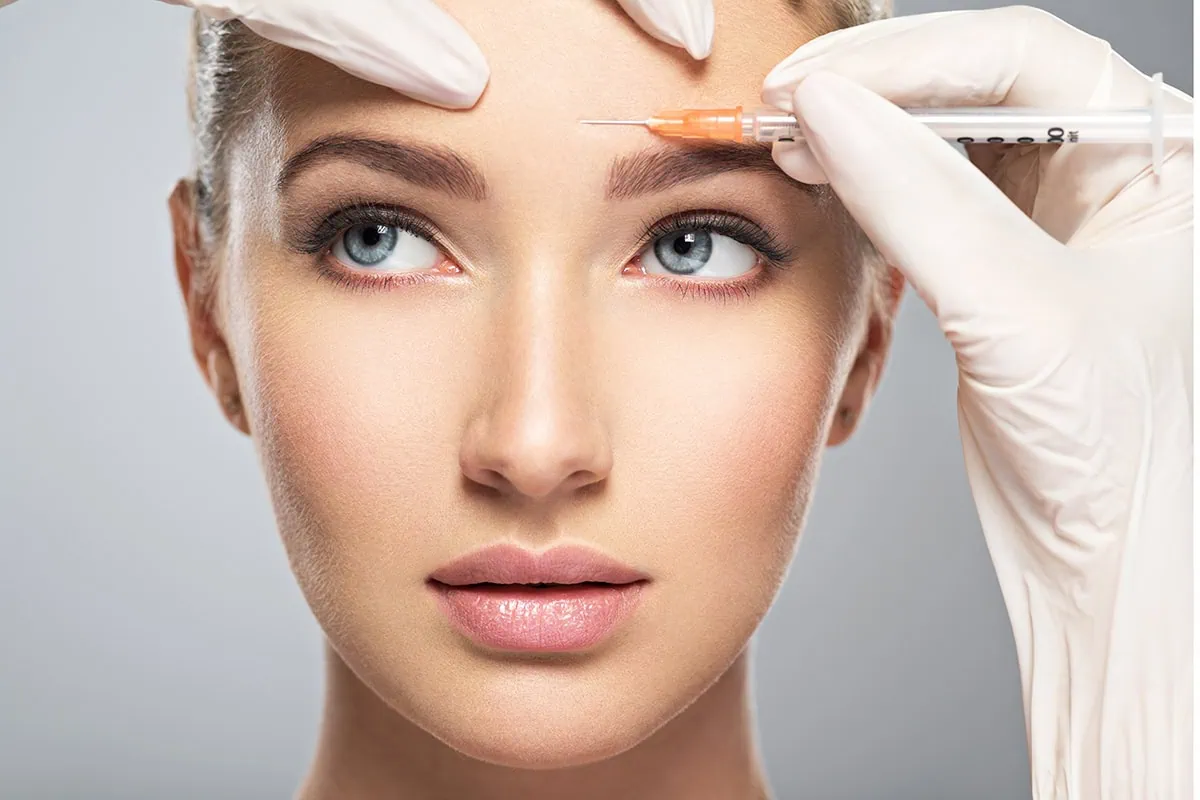 Young woman with beautiful skin getting a botox injection in her forehead.