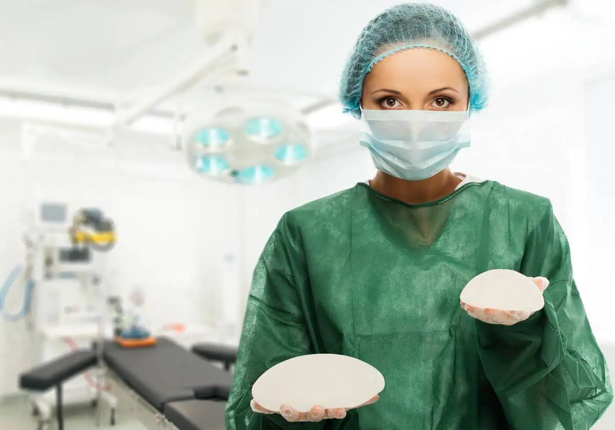 Doctor in scrubs holding two breast implants