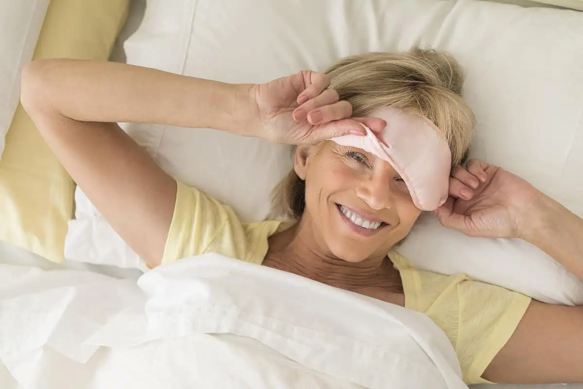 Woman smiling and peering out from a sleep mask