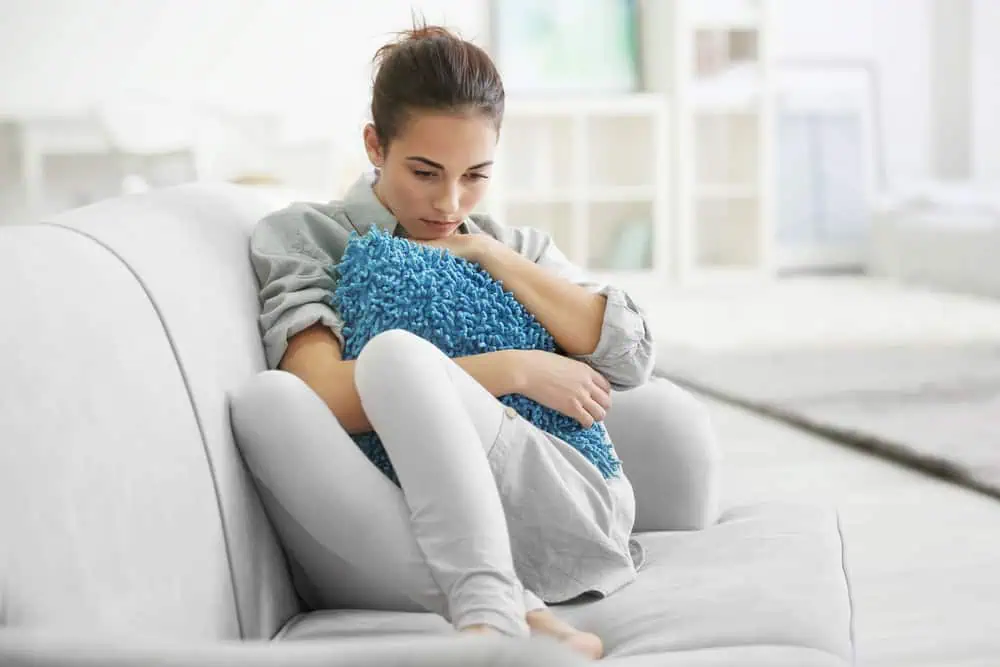 Woman sitting on a couch clutching a pillow.
